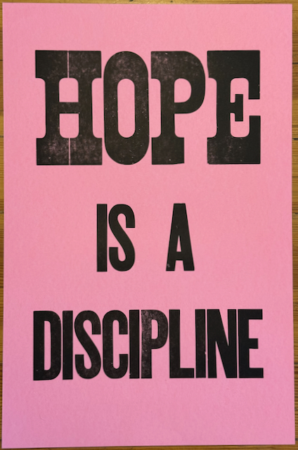 "HOPE IS A DISCIPLINE" printed with large wood type in black on pink paper
