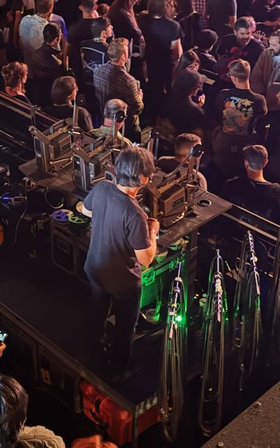 A person viewed from above standing behind four 16mm film projectors. To their right are racks of filmstrips.